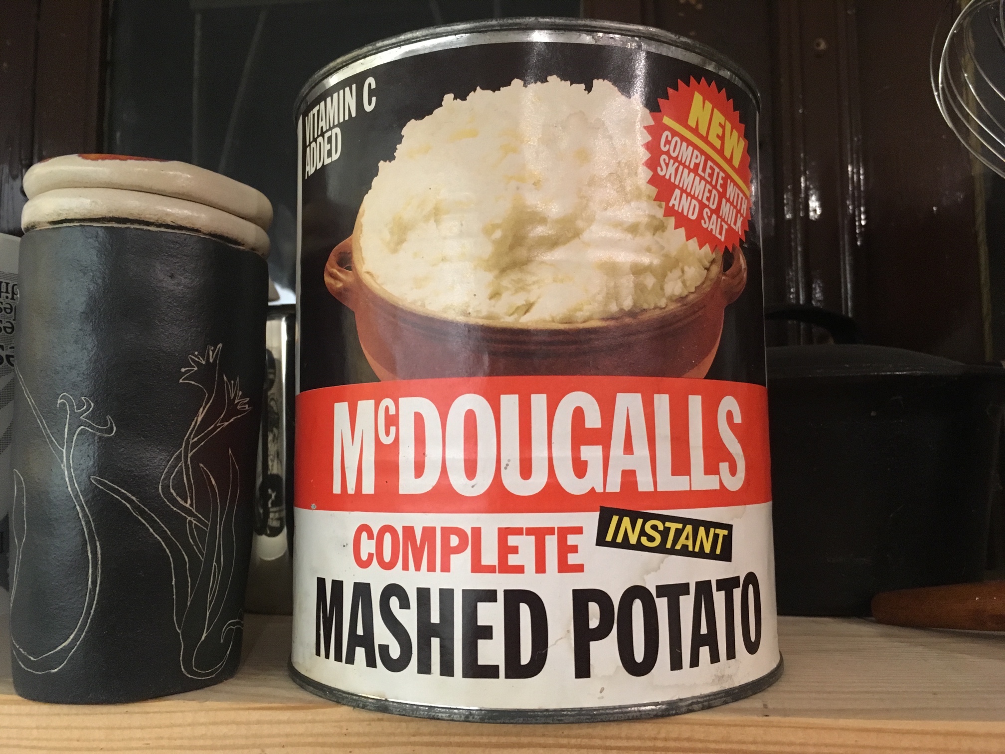 A huge, tin of “McDougals Instant Mashed Potato” sitting on a shelf