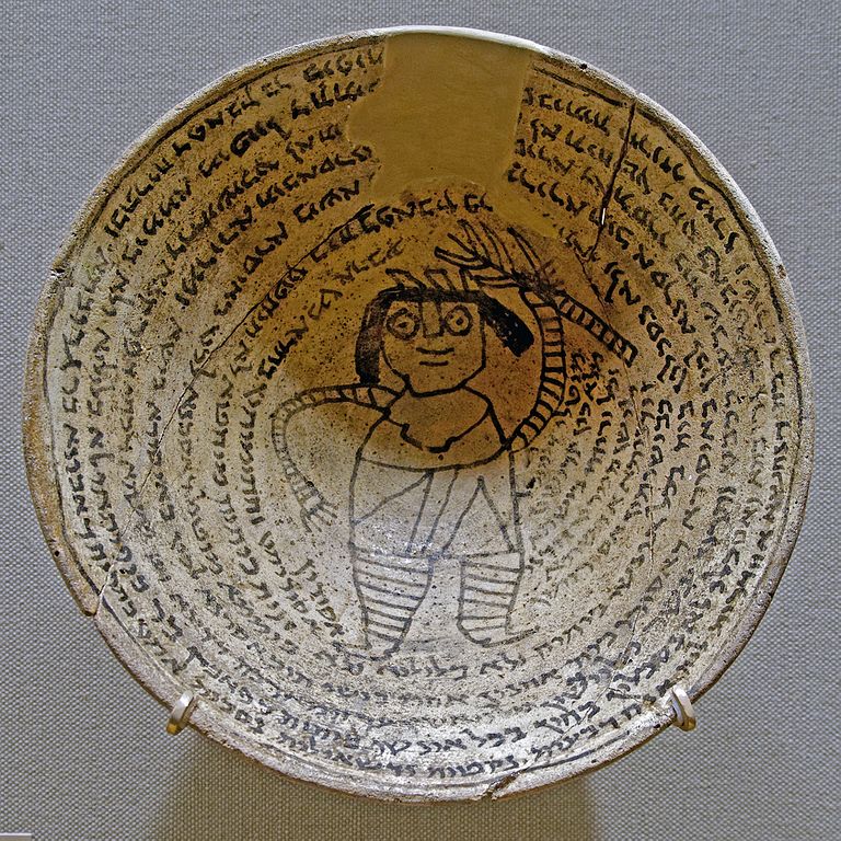 A ceramic bowl with text spiraling around the rim, and a line drawing of a smiling figure with bandaged limbs, holding a spiky stick above their head